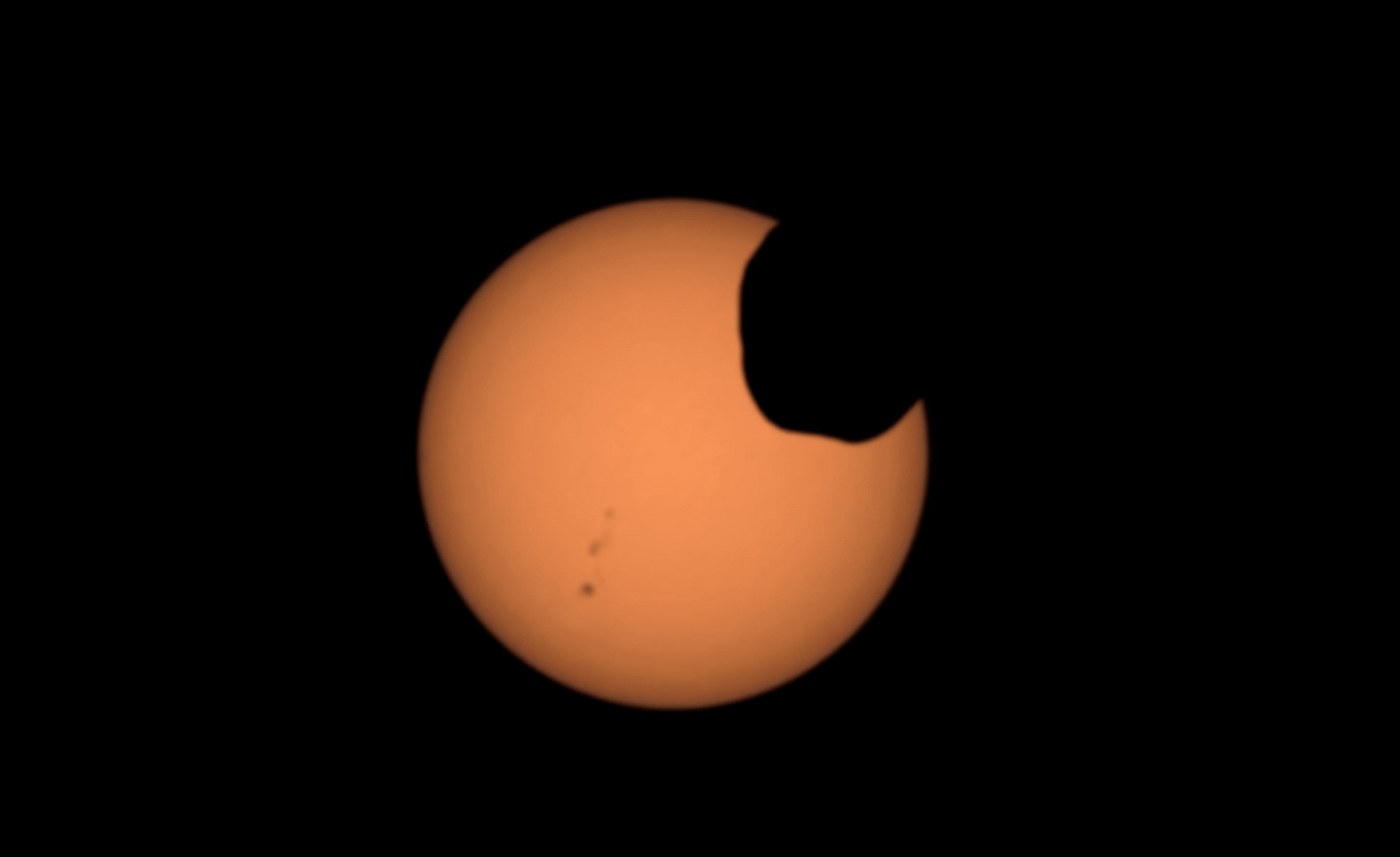 Mars� moon Phobos crosses the face of the sun, captured by NASA’s Perseverance rover with its Mastcam-Z camera. The black specks to the left are sunspots.