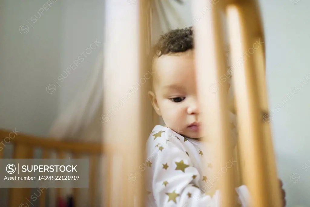 Baby boy standing up in crib looking down SuperStock