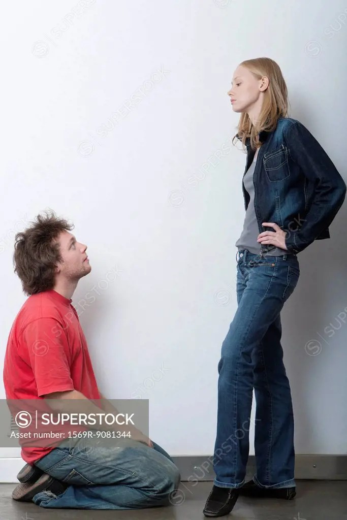 Young man kneeling in front of angry girlfriend SuperStock