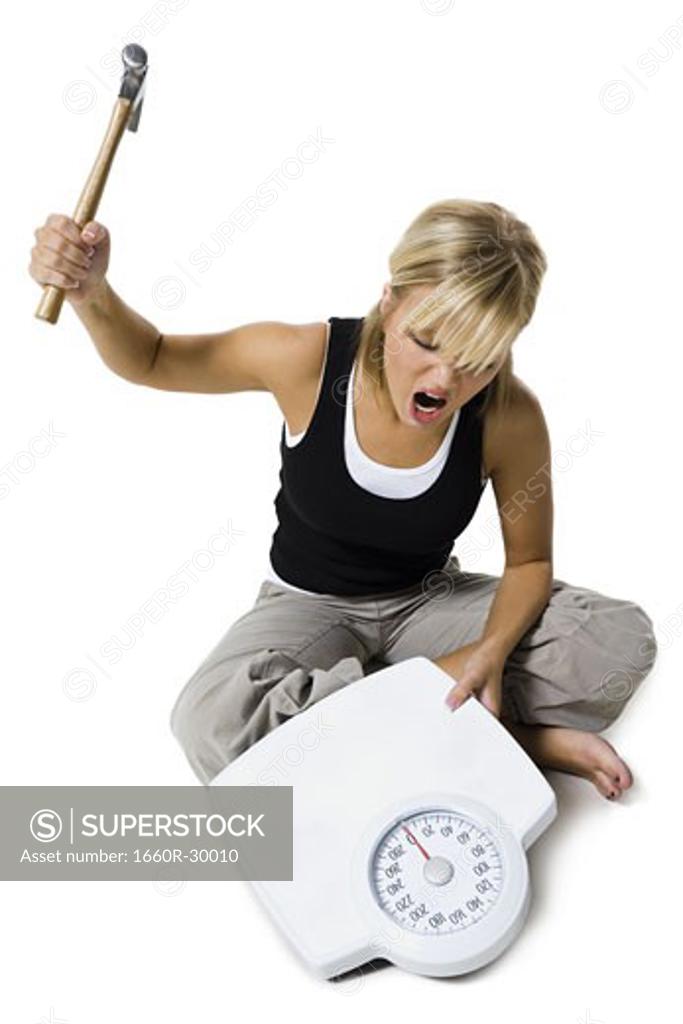 Frustrated dieting woman smashing bathroom scale with a hammer SuperStock