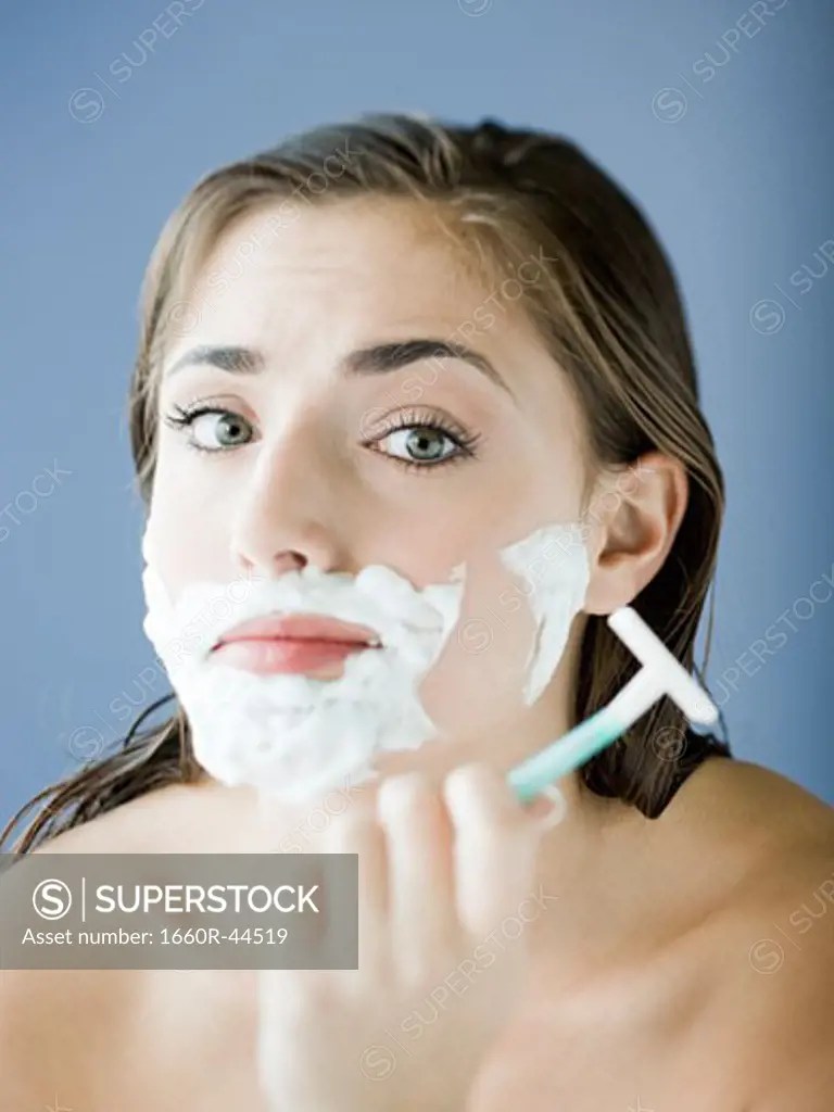 woman shaving her face with a razor and shaving cream SuperStock