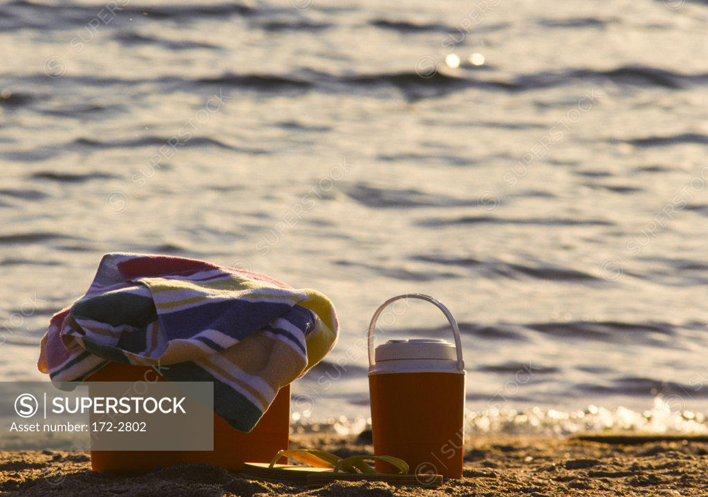 Picnic basket, thermos, flipflops and towel on beach SuperStock