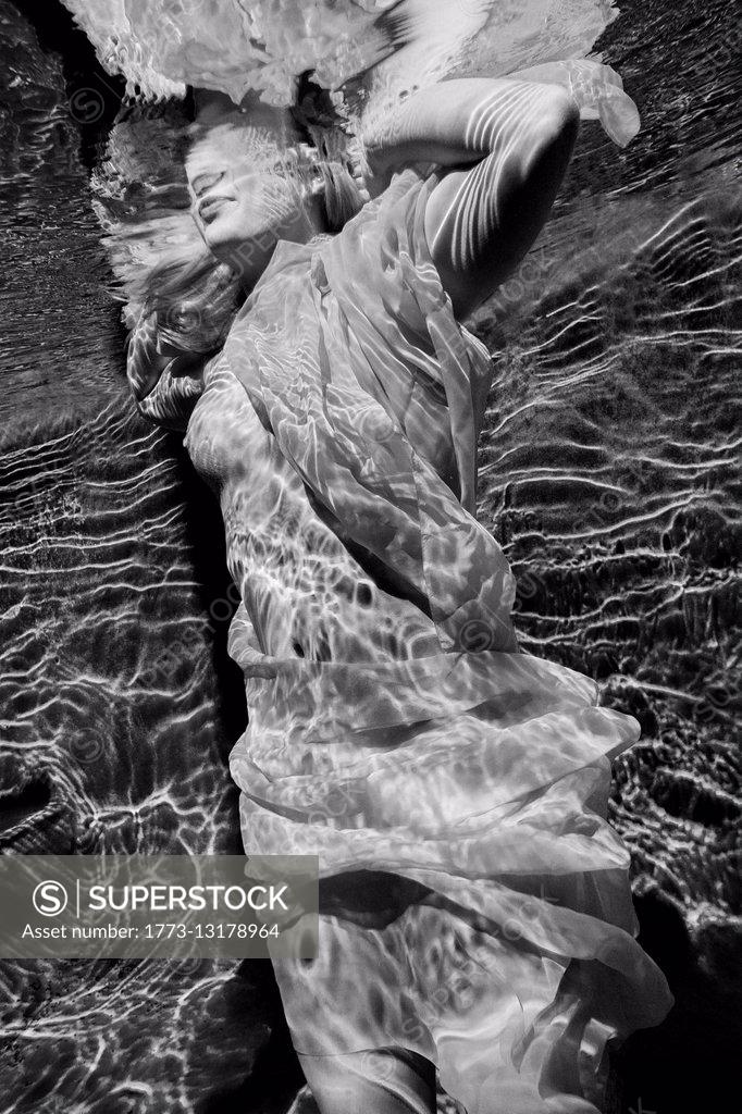 Woman draped in fabric swimming seminaked underwater SuperStock