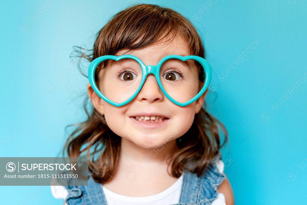 Portrait of cute little girl with heart shaped glasses on blue