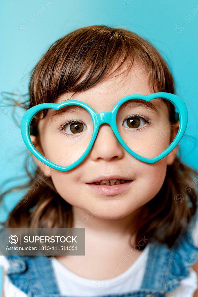 Portrait of cute little girl with heart shaped glasses on blue