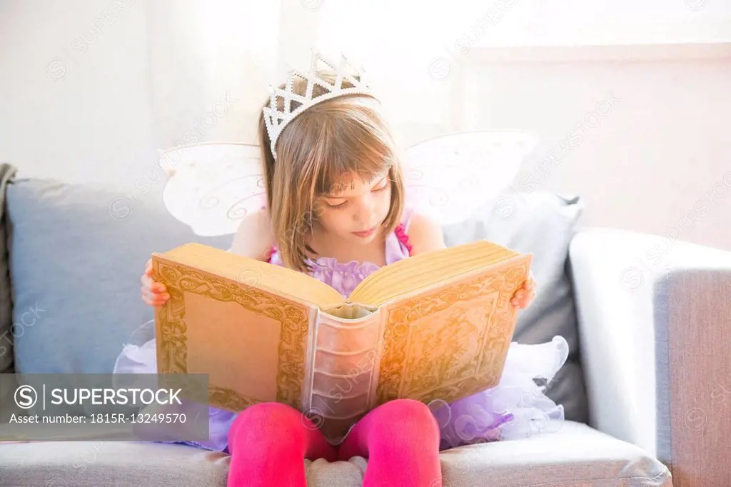 Portrait of little girl dressed up as fairy queen reading book SuperStock