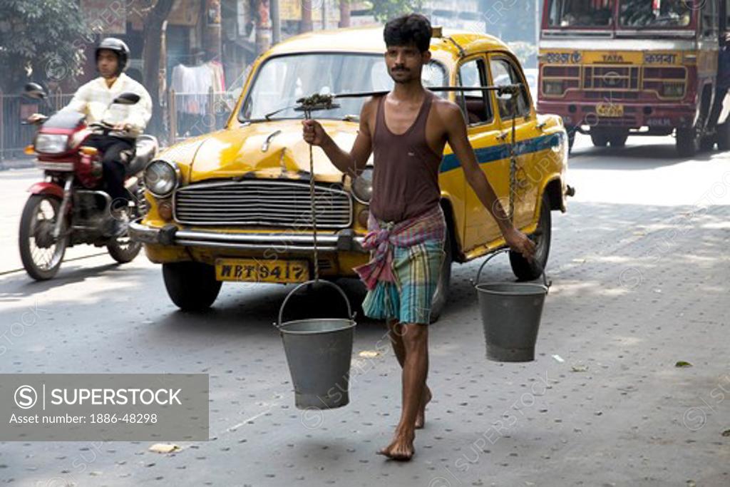 Man carrying water on shoulder in two buckets ; Park street ; Calcutta