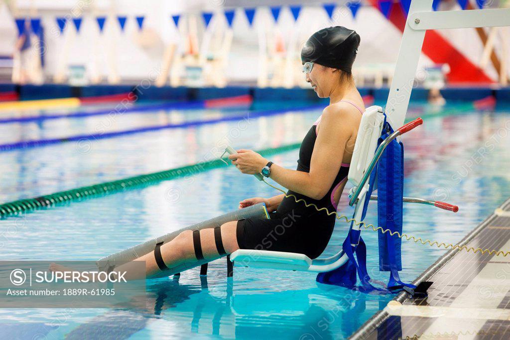 a paraplegic woman is lowered into the swimming pool on a lift and prepares to swim, edmonton
