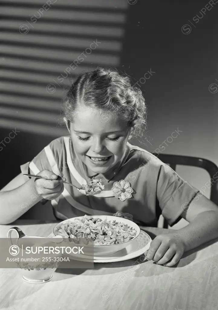 Girl eating corn flakes and smiling SuperStock