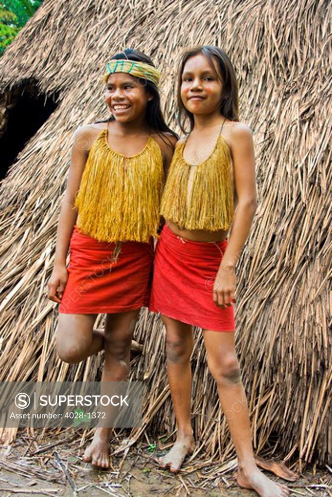 Two young girls stand outside of their tribal hut in the Peruvian