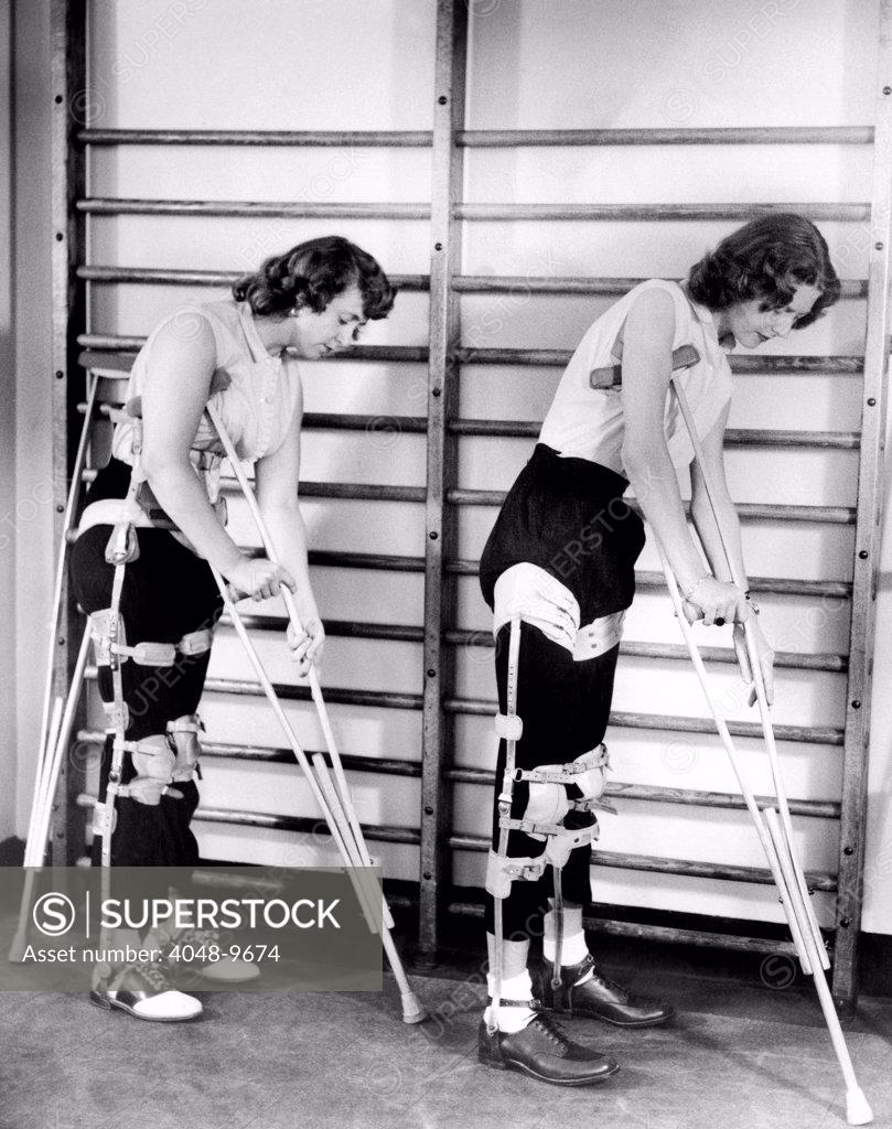 Two adult women polio victims with leg braces adjust their crutches