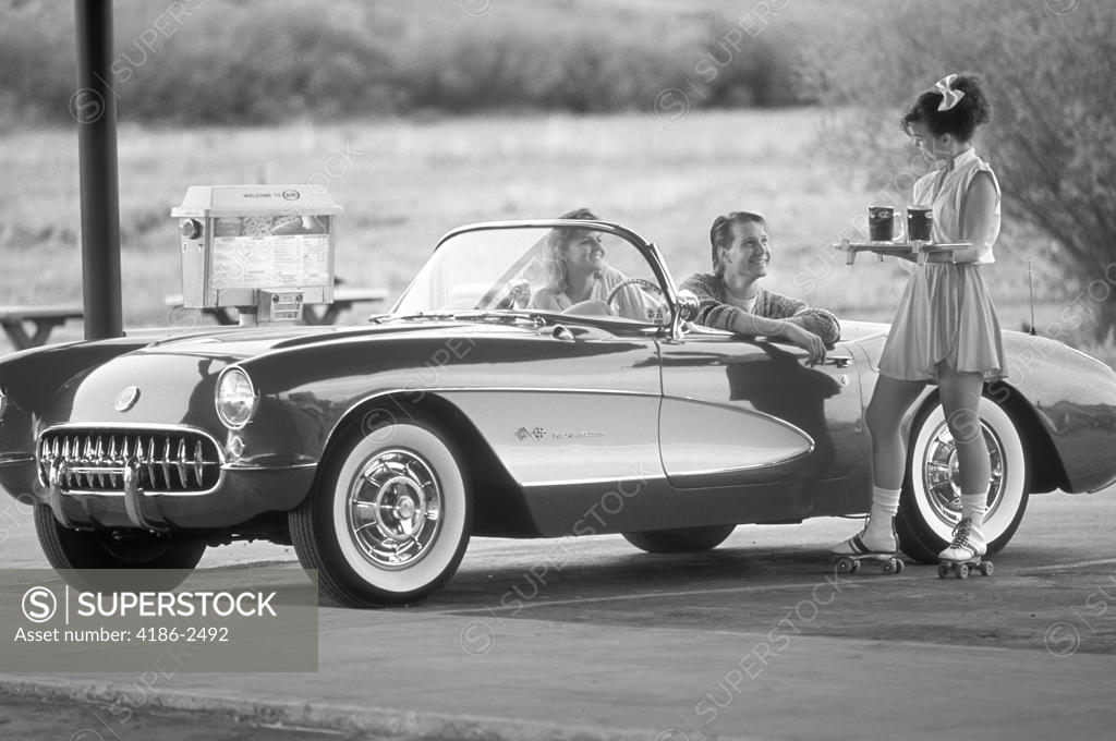 Carhop On Roller Skates Serving Drinks To Couple In Old Corvette