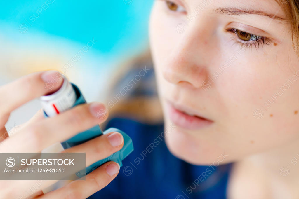 Asthma. Woman using an aerosol inhaler that contains bronchodilator for
