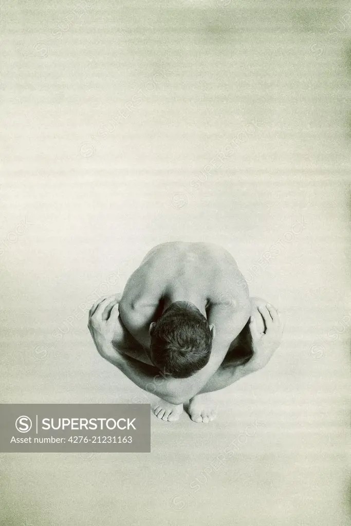 Nude man crouching with head down, hands on knees - SuperStock