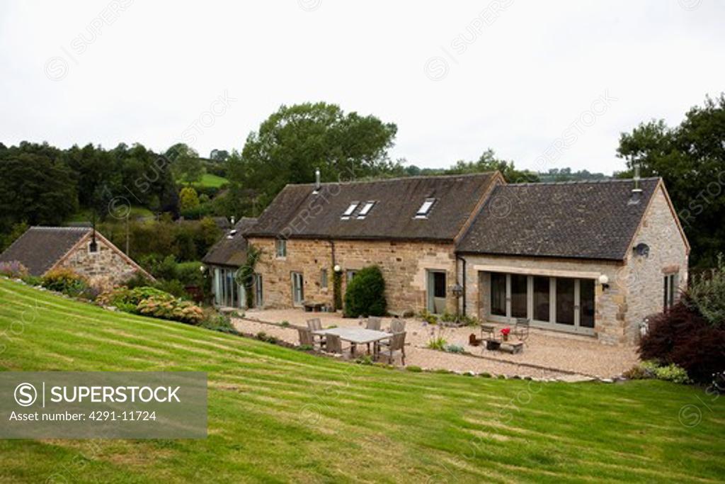 Sloping lawn down to traditional stone barn conversion with gravel terrace SuperStock