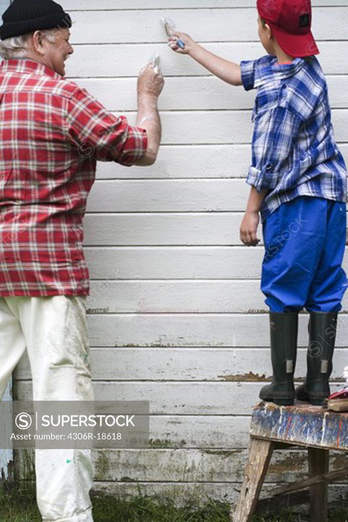 Grandfather and grandson painting their summer cottage, Sweden