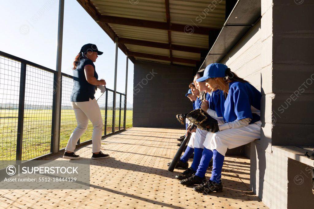 Diverse group of female baseball players sitting on bench, listening to
