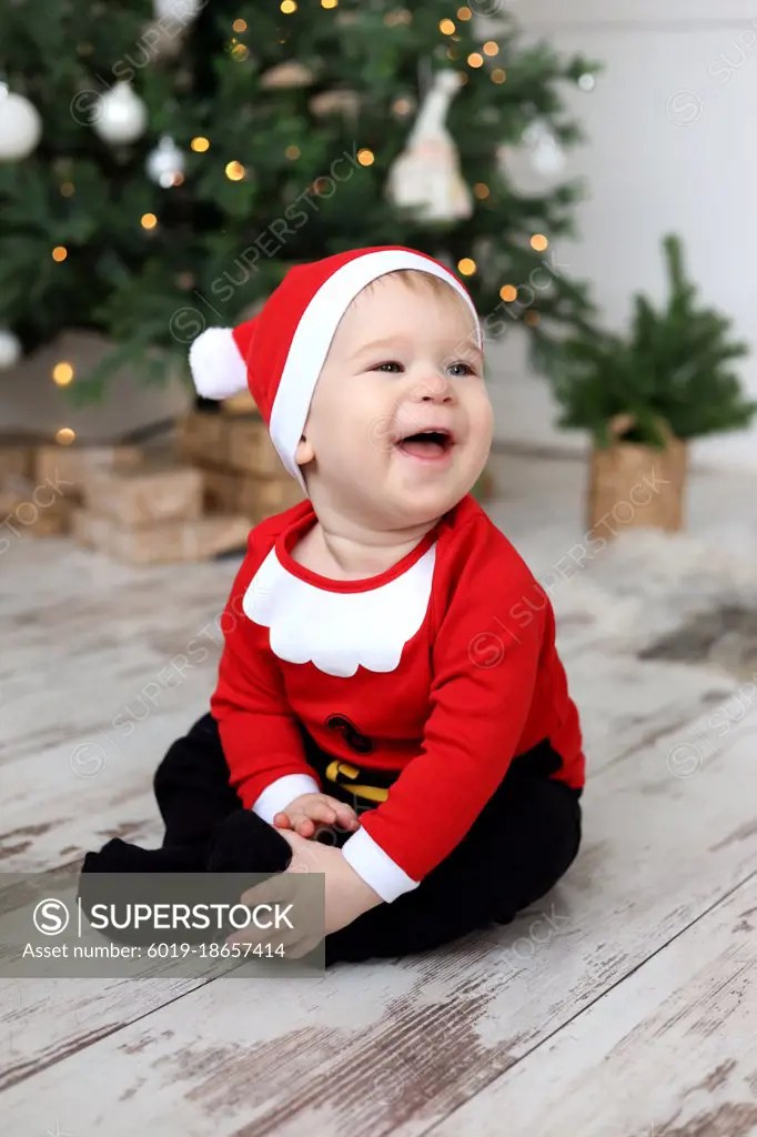 Baby boy in Santa Claus Costume is sitting on the floor and laughing