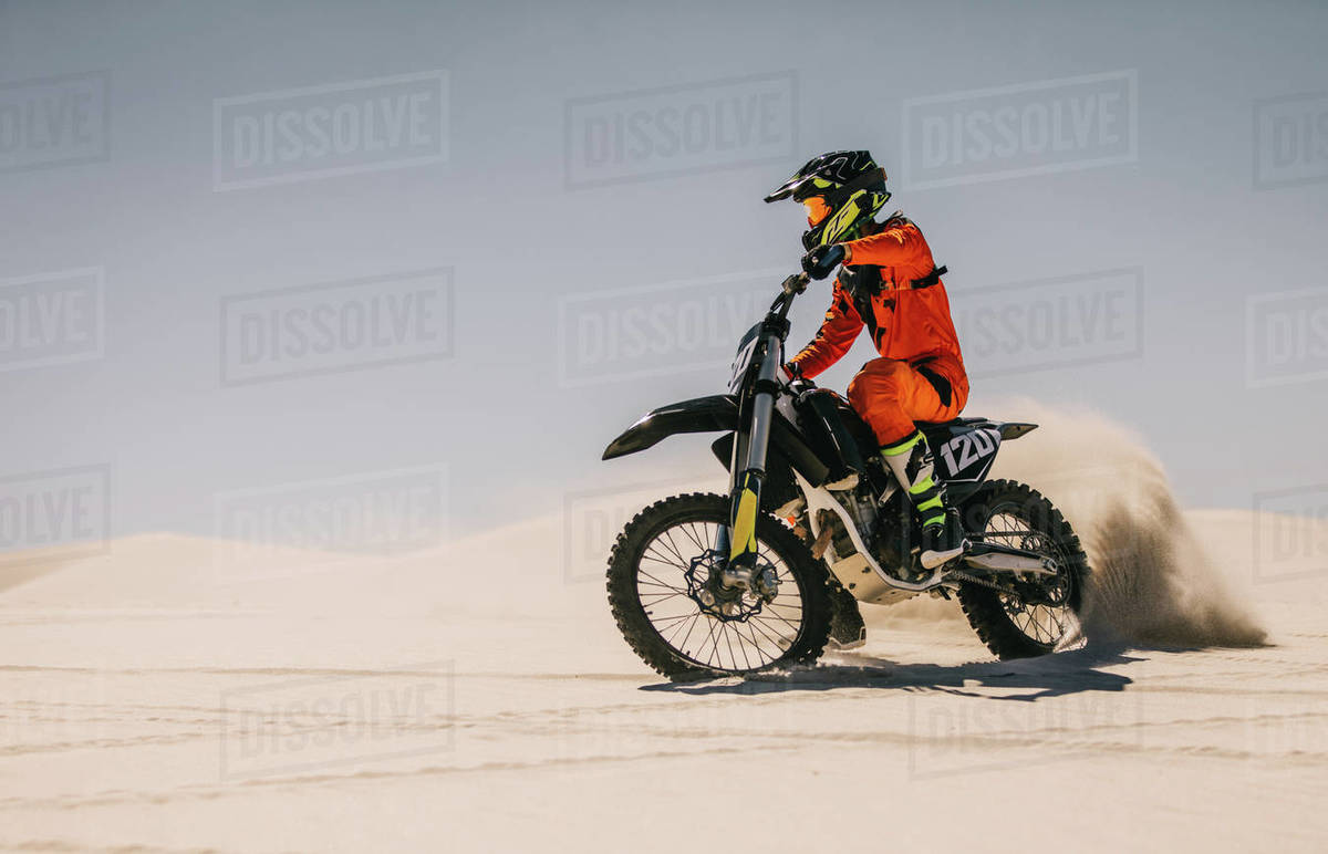 Motocross racer riding over sand in desert. Motocross biker driving