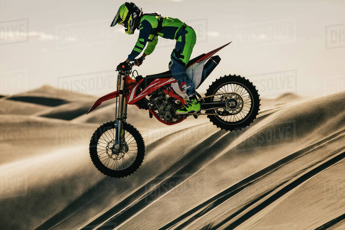 Motocross rider riding his racing bike down the sand dune. Professional