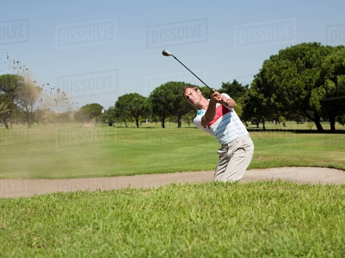 Man playing golf, stuck in bunker Stock Photo Dissolve