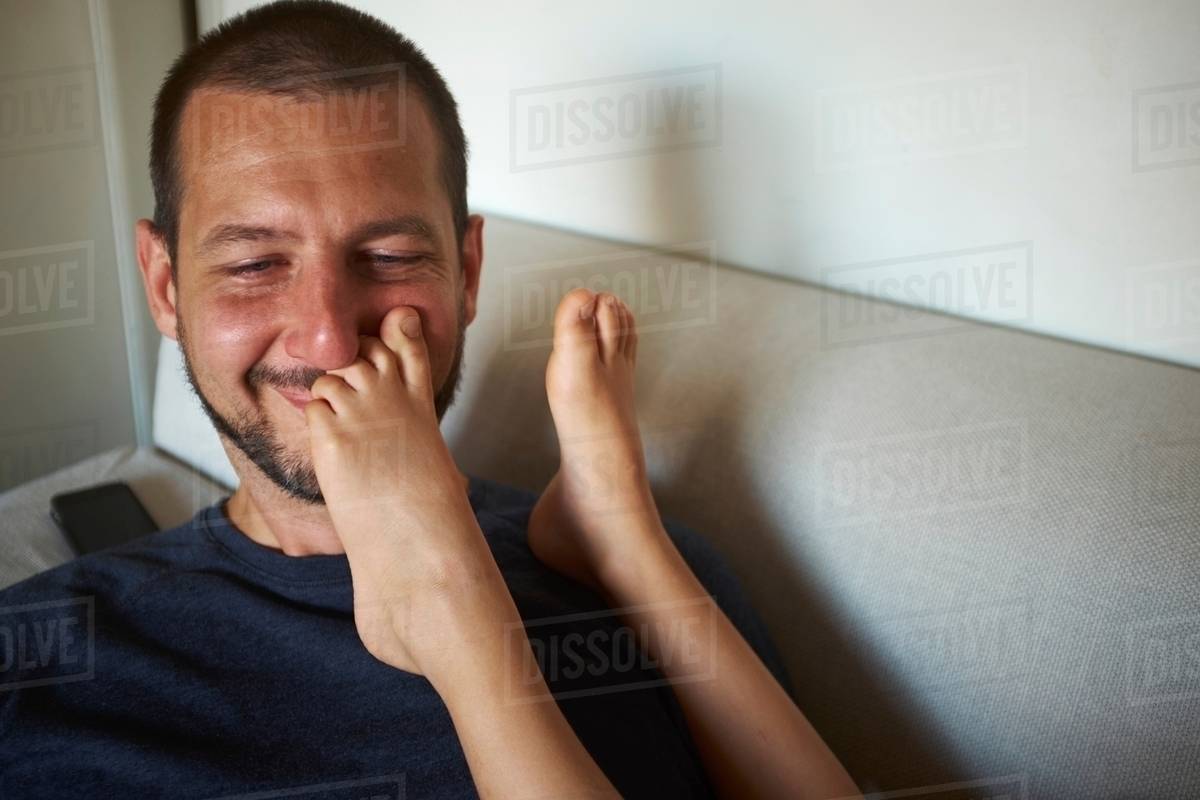 Father sitting on sofa, son's bare feet touching his face Stock Photo