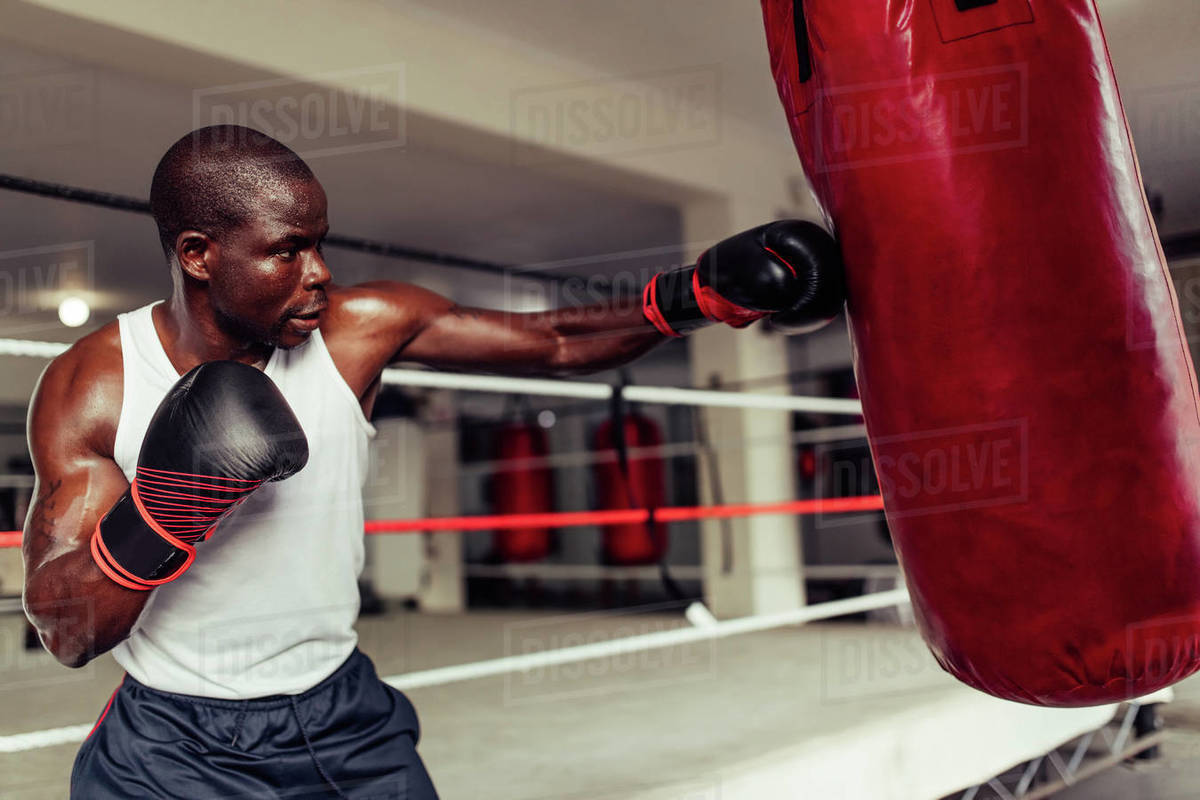 Fit muscular young African boxer throwing a powerful punch at a red