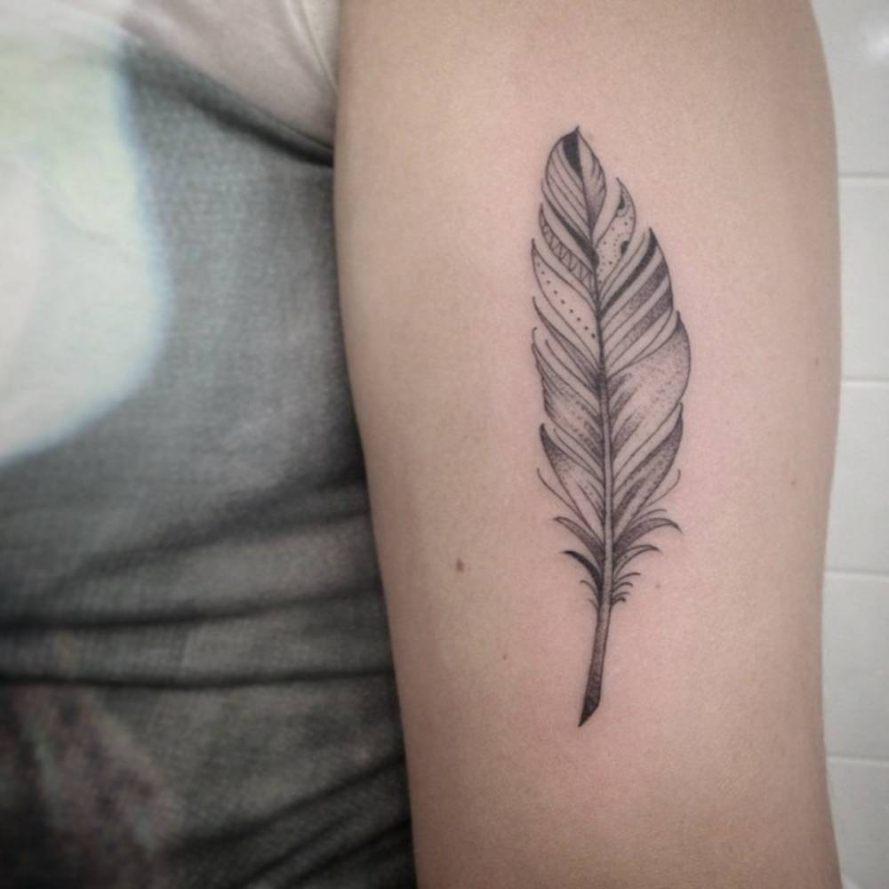 Feather tattoo on the upper arm by Ivy Saruzi.