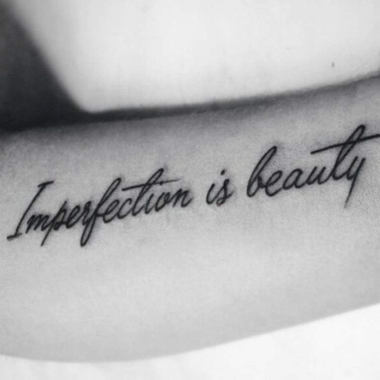 Tatuaje que dice "Imperfection is beauty", frase en