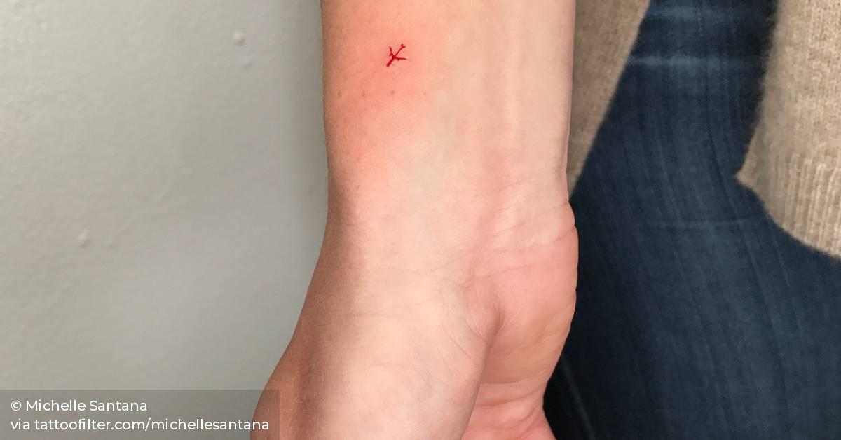 Small red ink plane tattoo on the wrist.