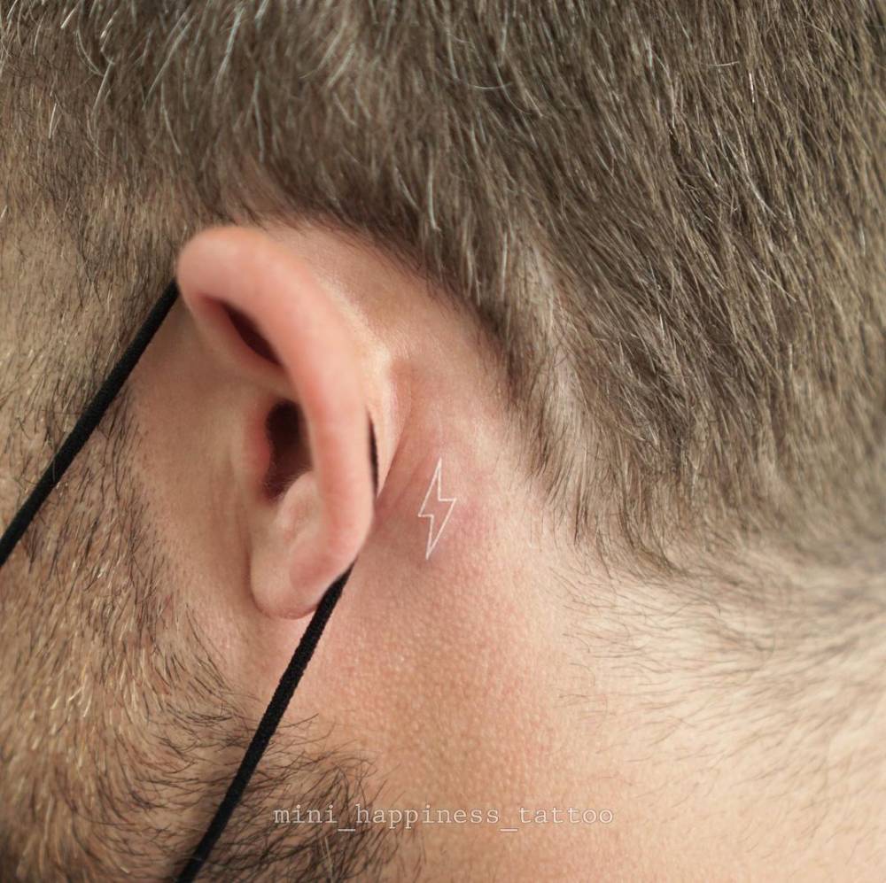 Tiny white lightning bolt tattoo located behind the