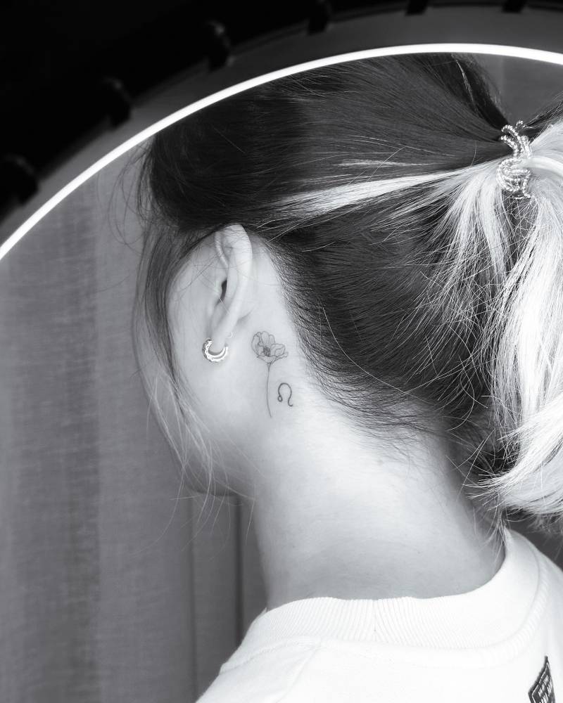 Fine line style poppy flower tattoo located behind the