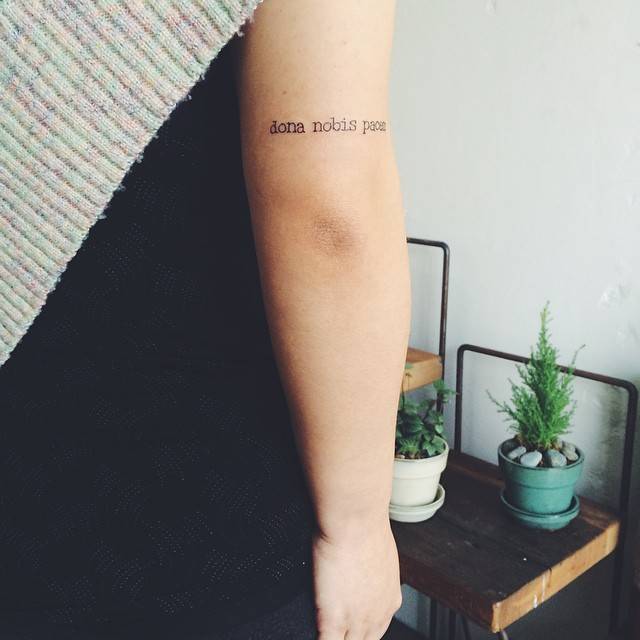 Tricep tattoo saying "Dona nobis pacem."
