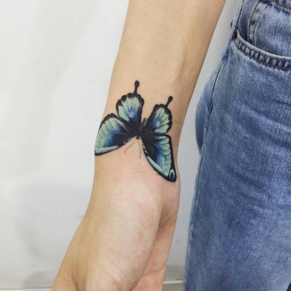 Blue butterfly tattoo on the right wrist.