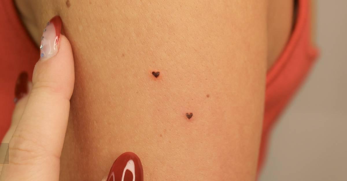 Tiny heart freckles tattoo located on the upper arm.