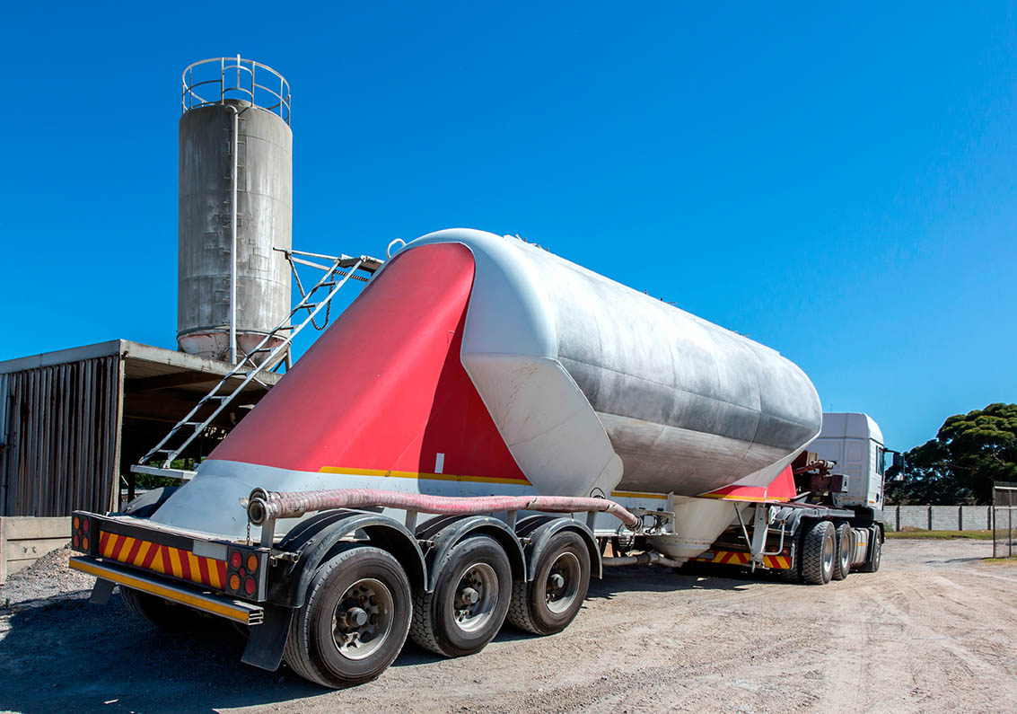 Cement delivery truck with multiple wheels and silo in backgroun Cemserve
