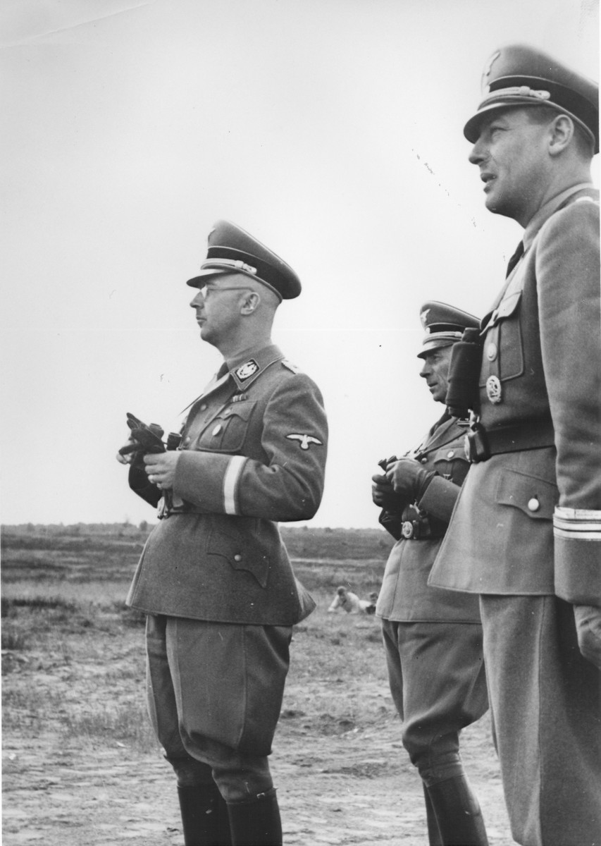 ReichsfuehrerSS Heinrich Himmler stands outside in a field holding a