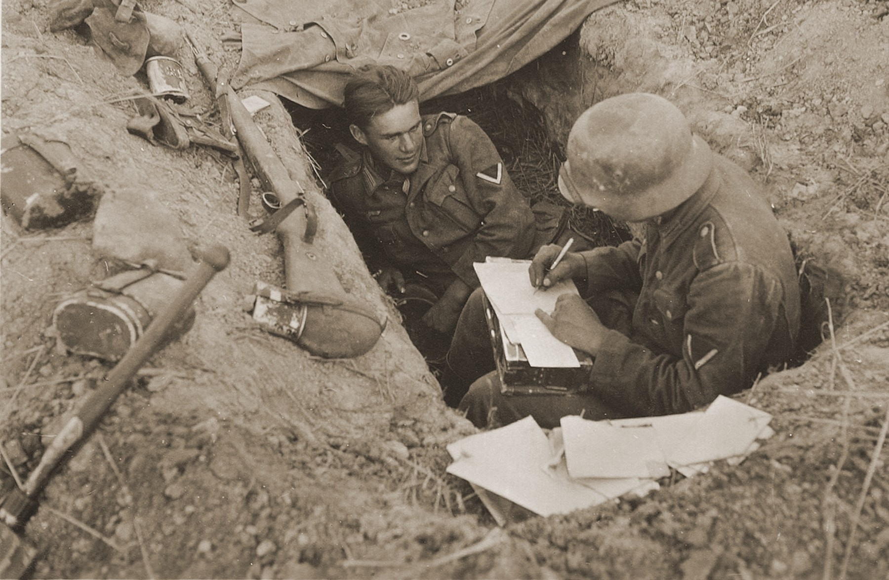 Two corporals in the German army rest in a foxhole during a lull in the