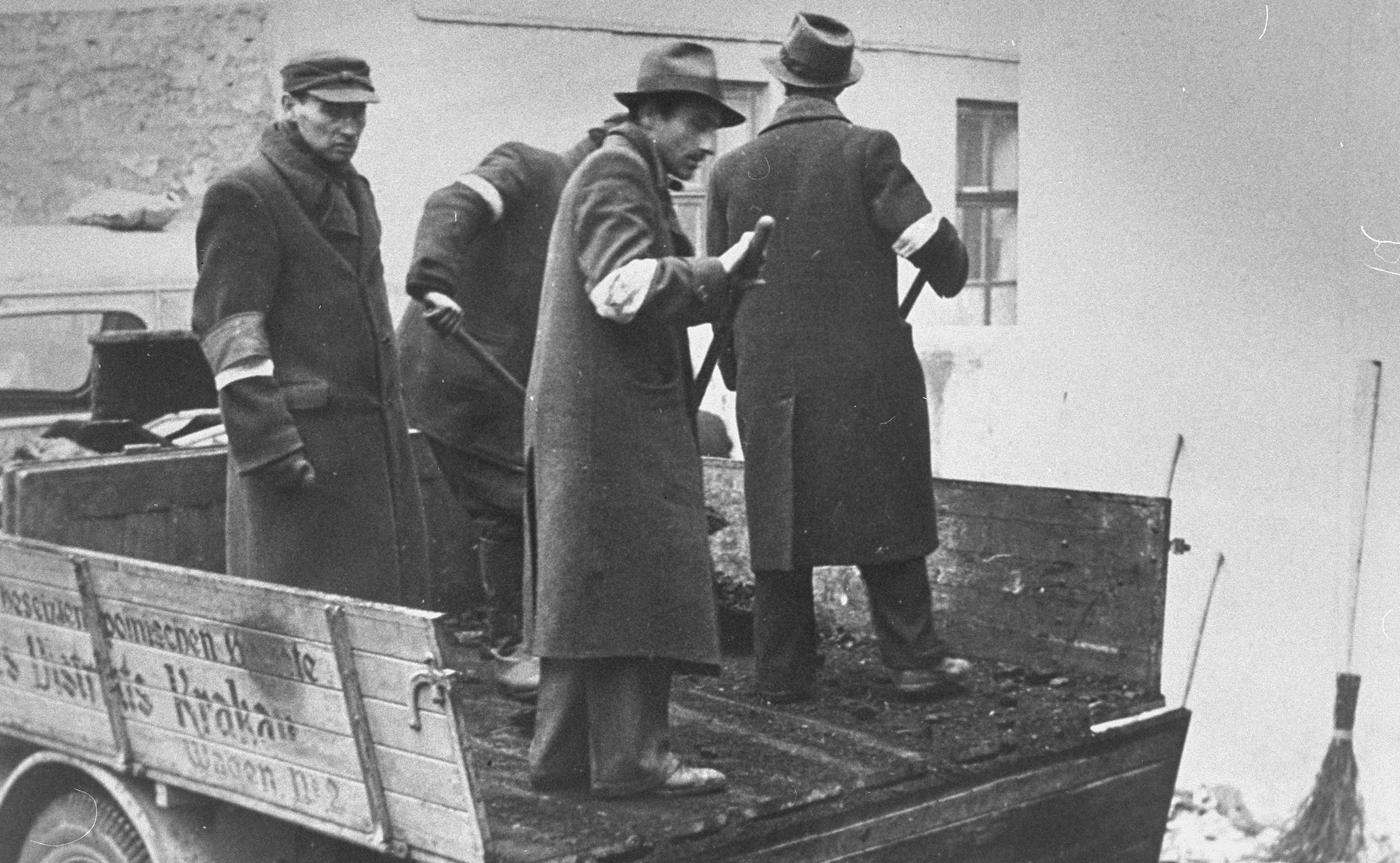 A group of Jewish men wearing armbands, shovel coal off the back of a