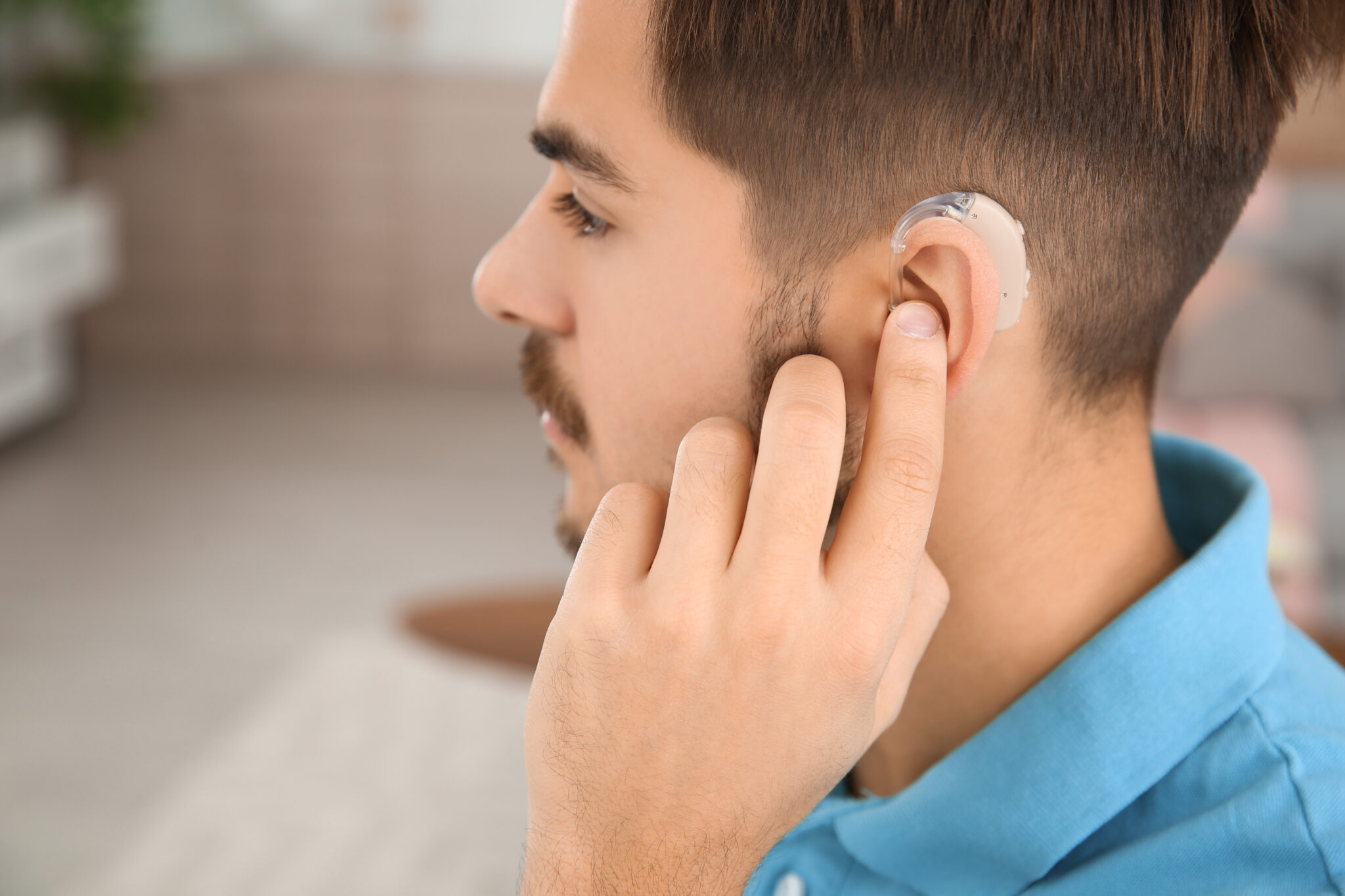 Young man adjusting hearing aid at home, closeup Compliance Standard