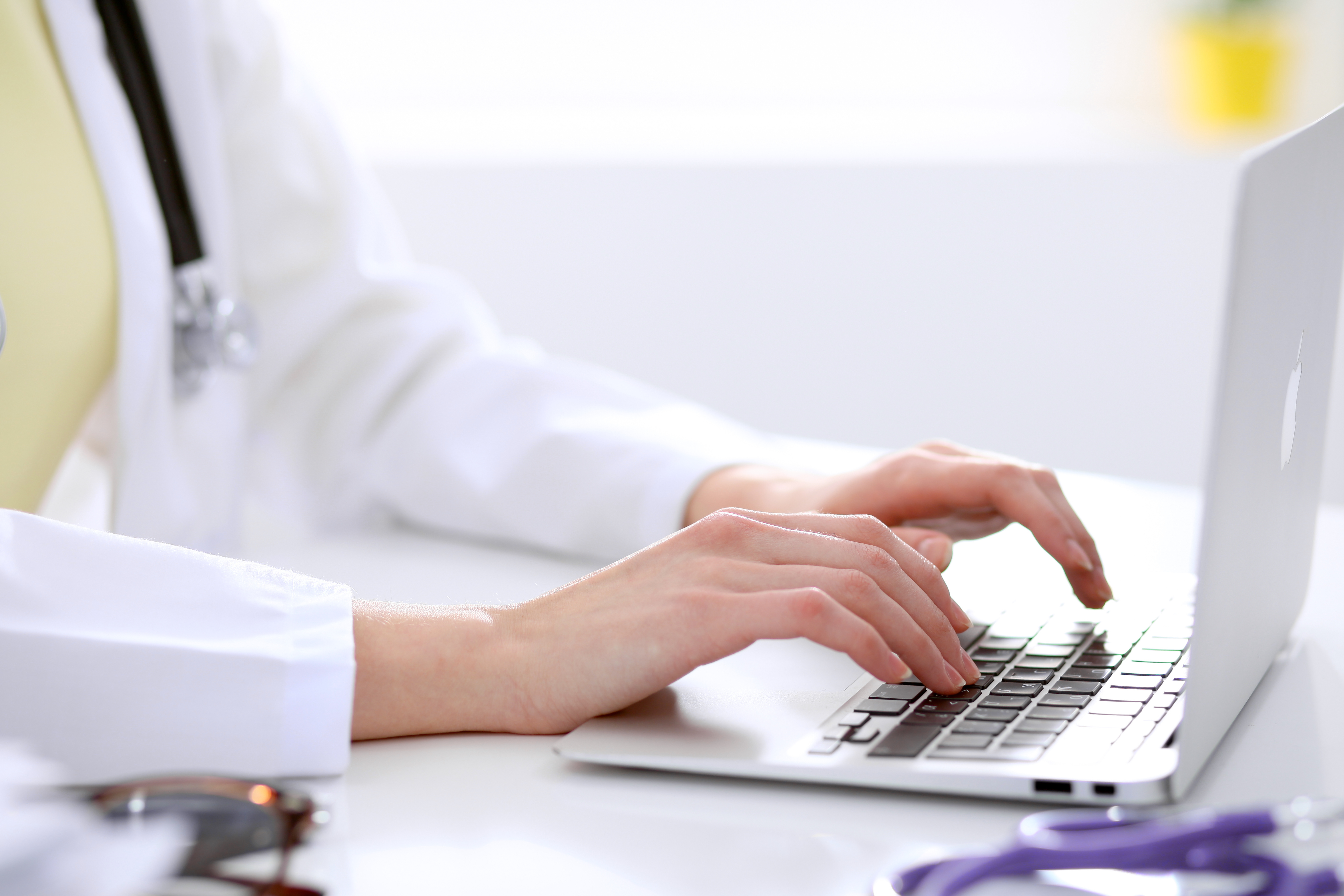 Closeup of female doctor typing laptop sitting at a table in the