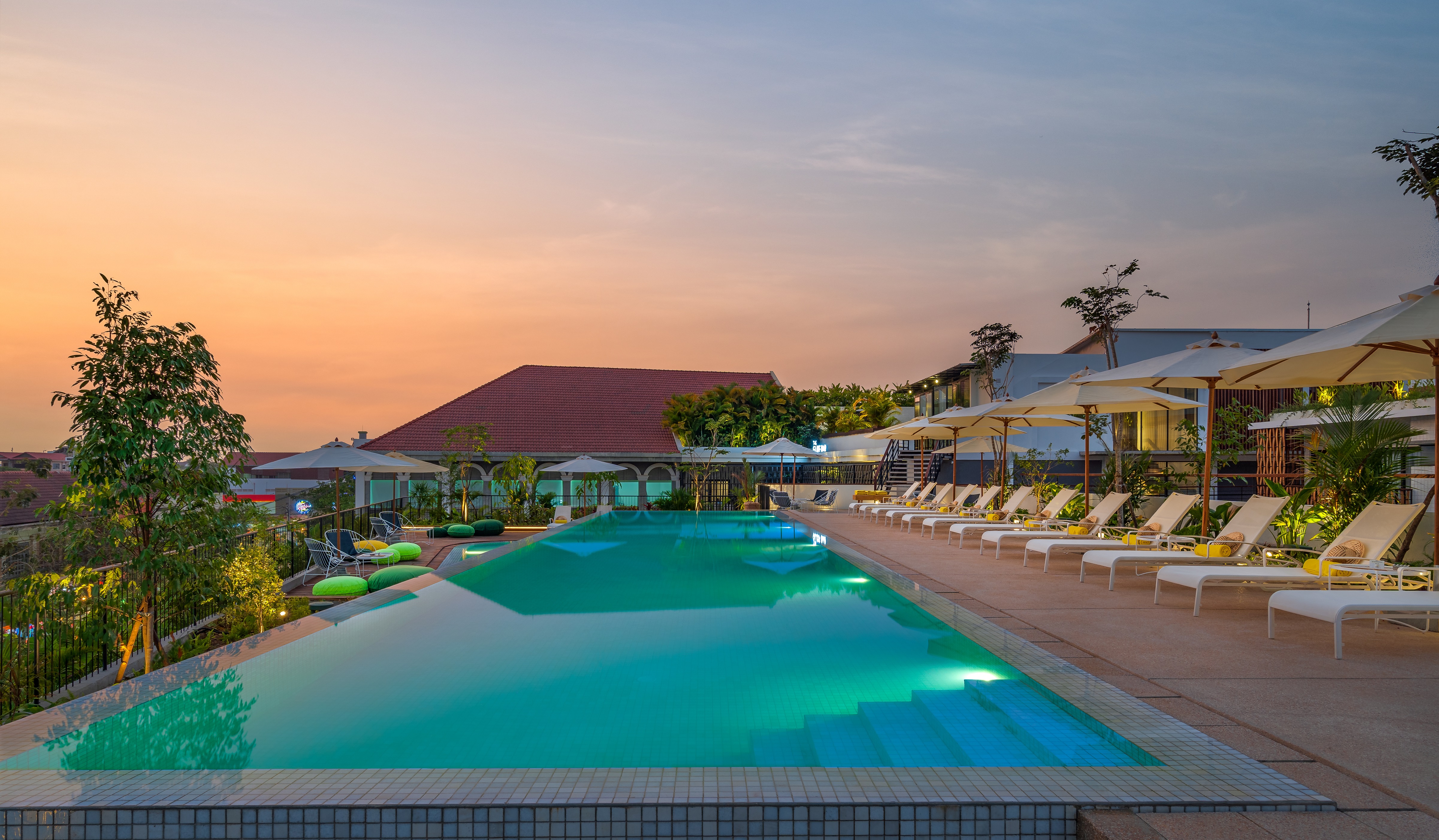 Travel public relations client The Aviary Hotel's Rooftop Pool with glowing sunset, lit pool, deck chairs and umbrellas