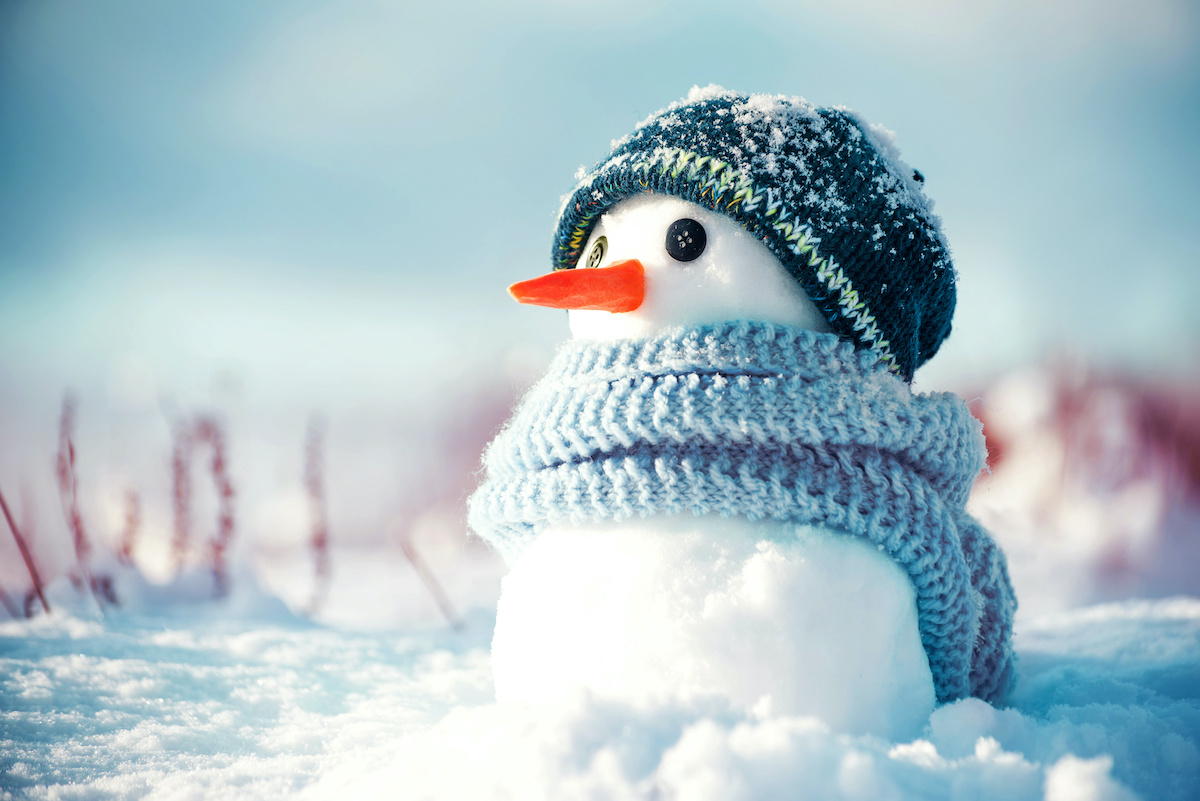 Little cute snowman in a knitted hat and scarf on snow on a sunny