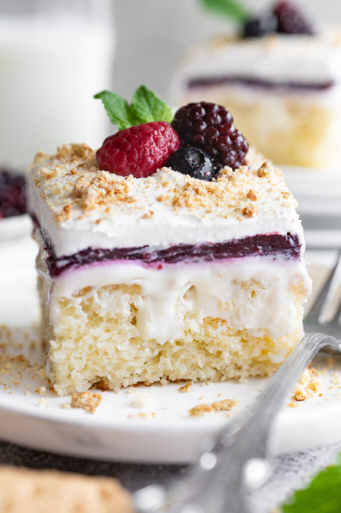 A triple berry cheesecake poke cake on a white plate.