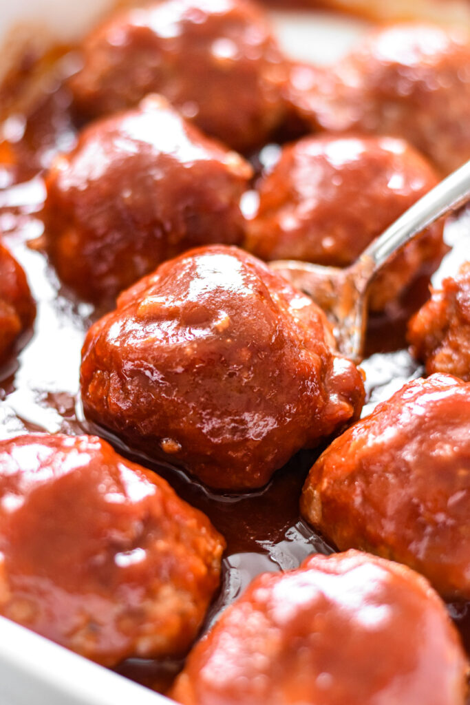 A siler spoon serving a ham ball from a white baking dish.