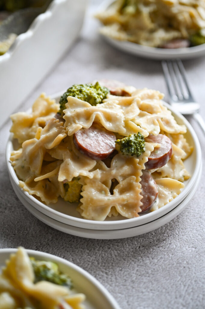 A white plate with a sausage and broccoli pasta in a creamy sauce with a fork next to it.