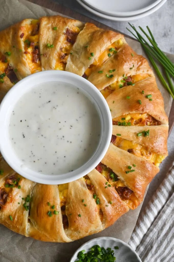 A breakfast crescent ring with a bowl of white gravy in the middle.