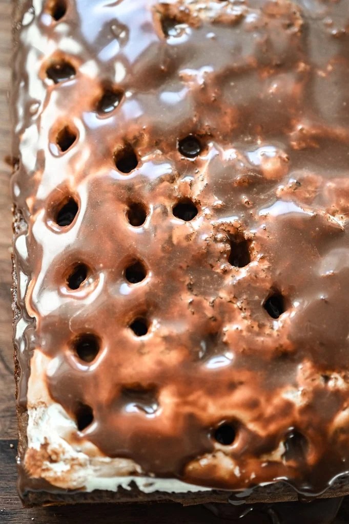 A poke cake with marshmallow filling and chocolate ganache sinking into the holes.
