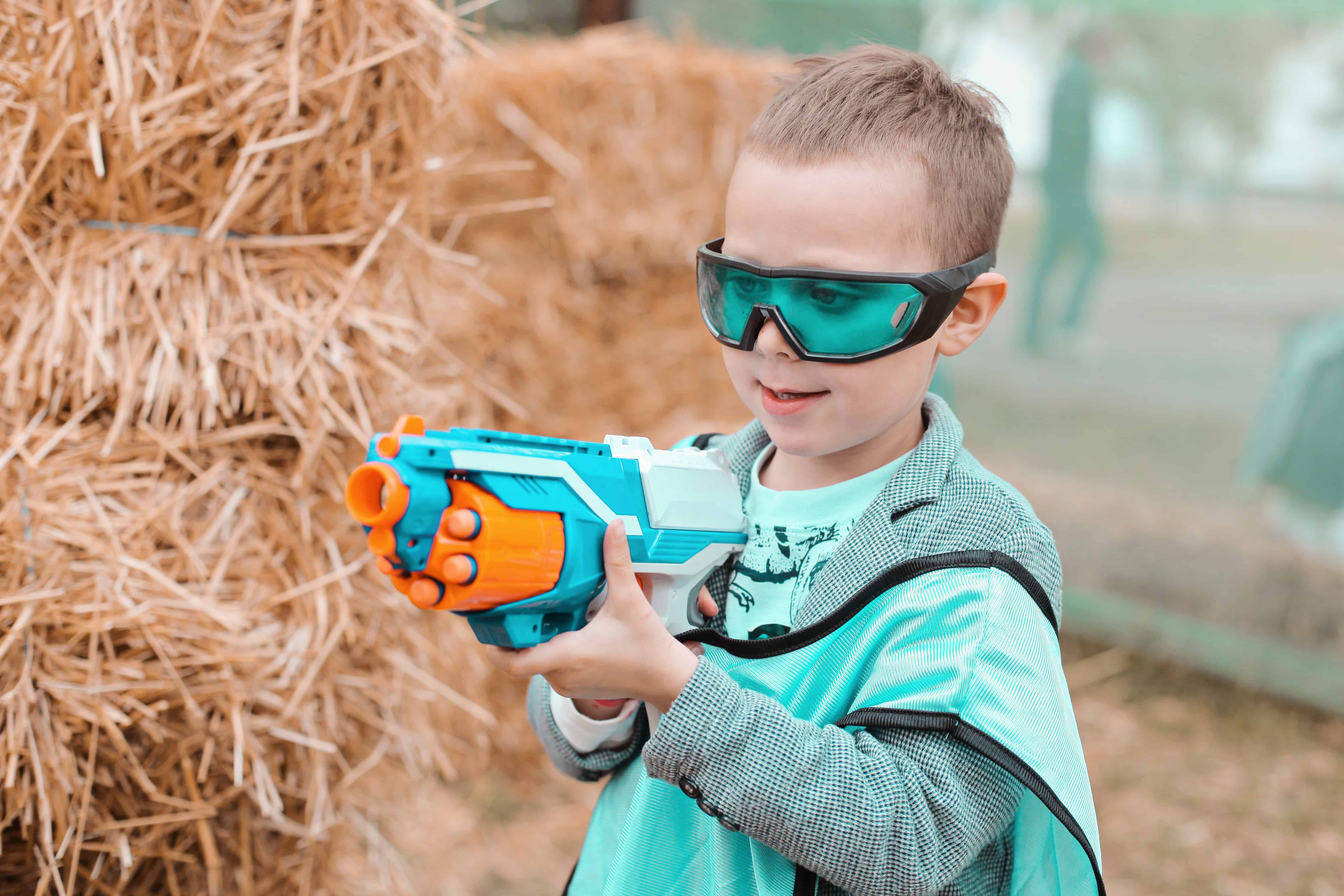 Small preschooler boy with blaster prepare for attack and play with