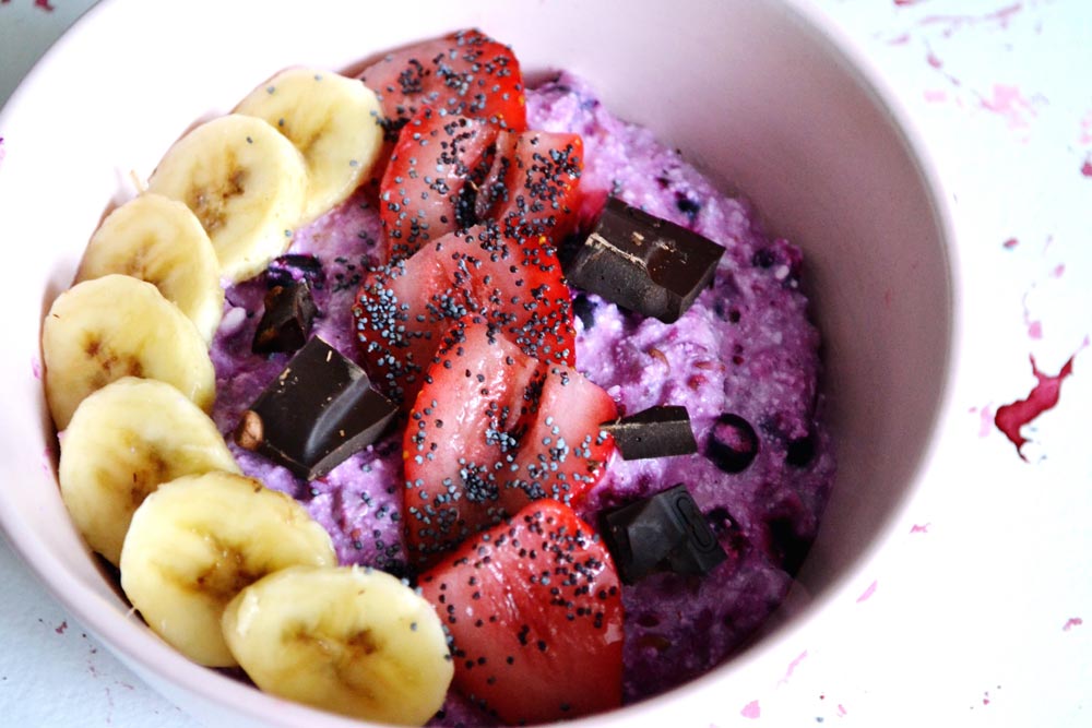 Close up view of white below with sliced bananas, sliced strawberries on top of purple yogurt.